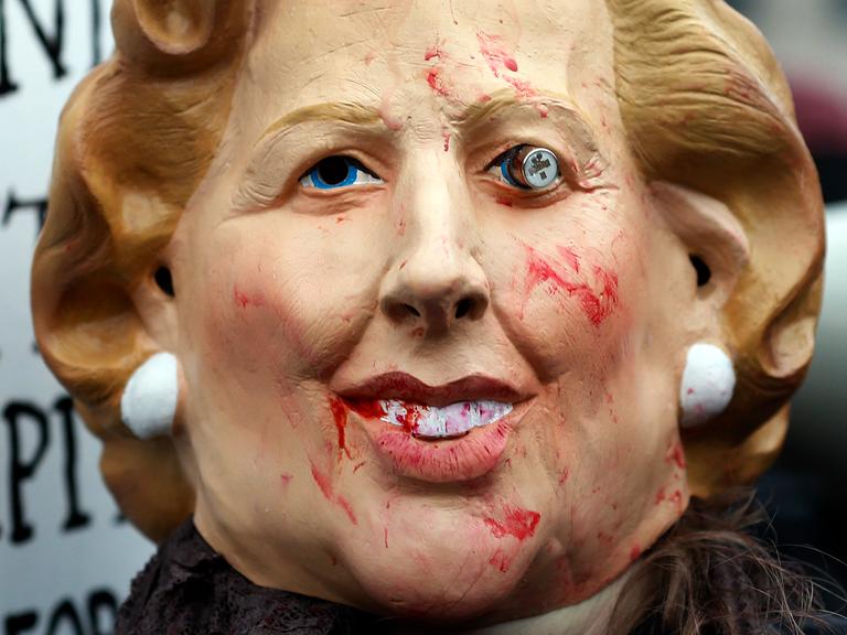 Das Bild zeigt eine verunstaltete Maske, die die ehemalige britische Premierministerin  Margaret Thatcher darstellen soll. Das Gesicht ist mit Blut beschmiert, ein Auge hängt aus der Augenhöhle.