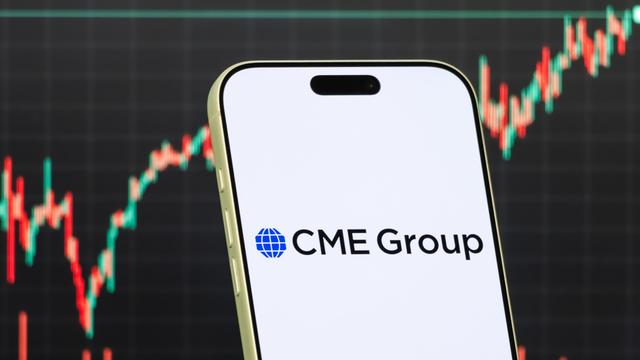 Diese Fotomontage zeigt das Logo der CME Group auf einem Smartphone vor einem Bildschirm, der den aktuellen Aktienmarkt-Chart des Unternehmens anzeigt. 