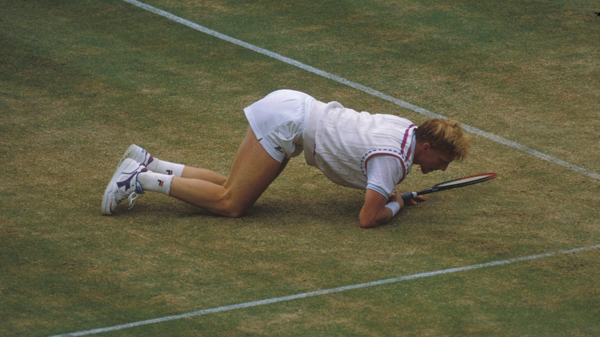 Boris Becker halb kniend, halb liegend auf dem Rasen-Court von Wimbledon. Er blickt dabei direkt auf den Schlägerkopf.