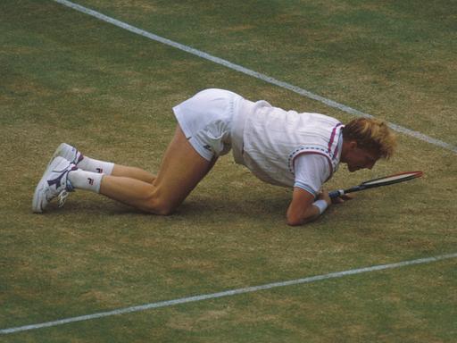 Boris Becker halb kniend, halb liegend auf dem Rasen-Court von Wimbledon. Er blickt dabei direkt auf den Schlägerkopf.