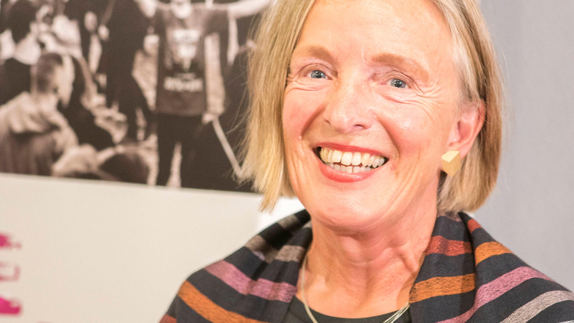 Porträt von Ute Frevert vor Aufstellern einer Ausstellung. Sie trägt dunkle Kleidung und lacht in die Kamera. Porträt von Ute Frevert vor Aufstellern einer Ausstellung. Sie trägt dunkle Kleidung und lacht in die Kamera.