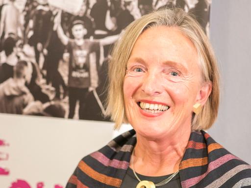 Porträt von Ute Frevert vor Aufstellern einer Ausstellung. Sie trägt dunkle Kleidung und lacht in die Kamera.