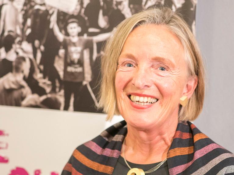 Porträt von Ute Frevert vor Aufstellern einer Ausstellung. Sie trägt dunkle Kleidung und lacht in die Kamera.