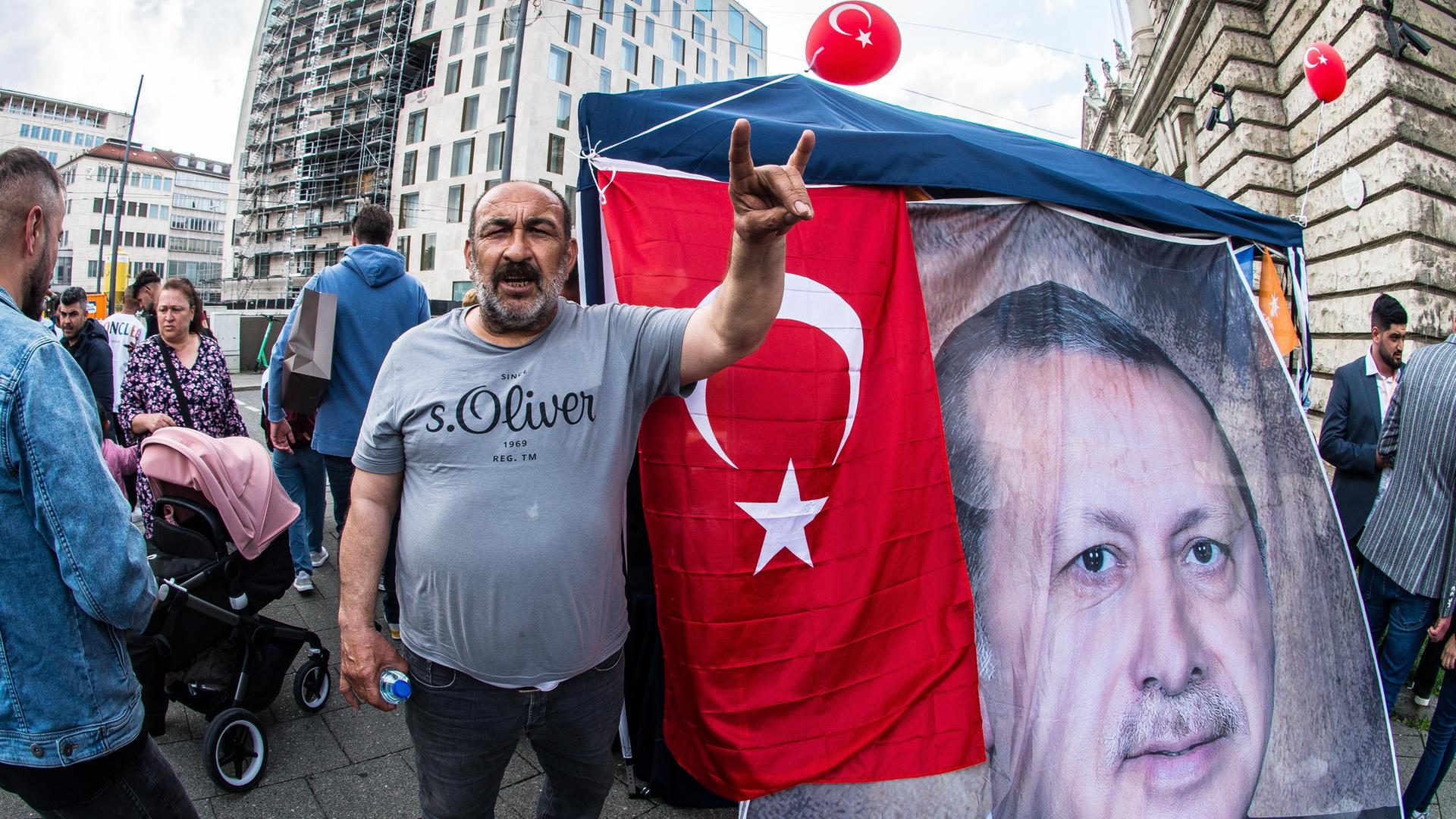 Ein Mann steht neben einem Transparent des türkischen Staatschefs Erdogan und zeigt den so genannten Wolfsgruß