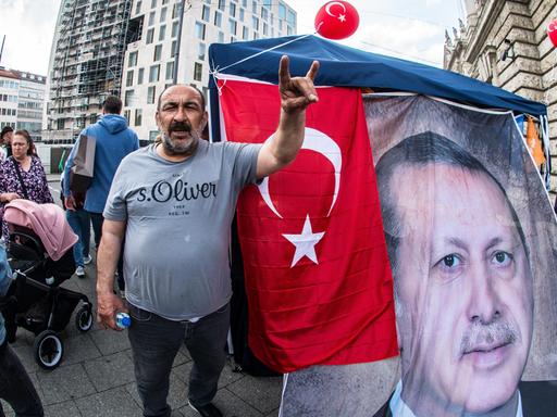 Ein Mann steht neben einem Transparent des türkischen Staatschefs Erdogan und zeigt den so genannten Wolfsgruß