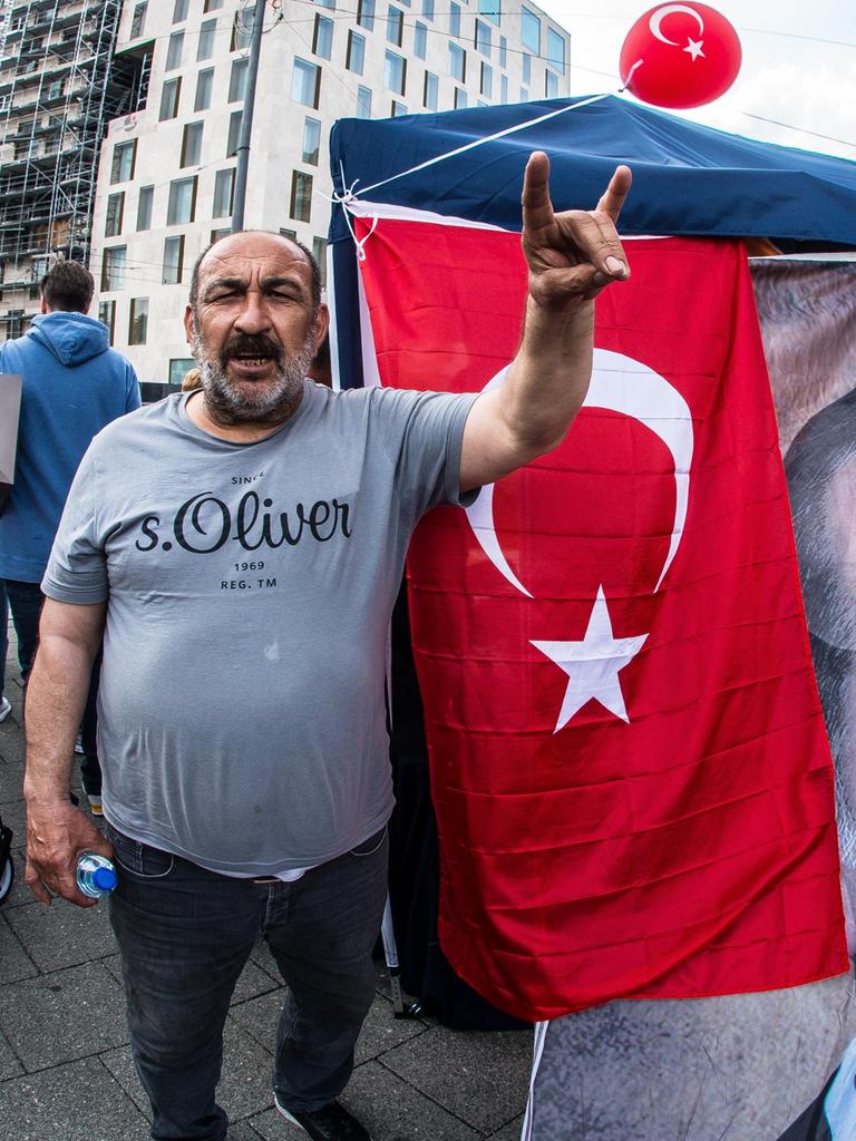 Ein Mann steht neben einem Transparent des türkischen Staatschefs Erdogan und zeigt den so genannten Wolfsgruß