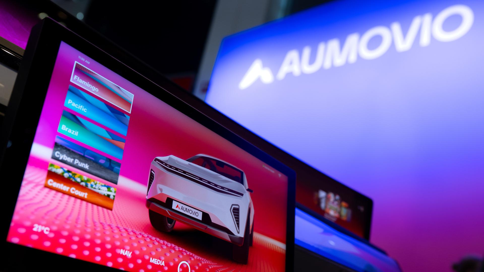 Das Bild zeigt ein elektronisches Display mit einem Auto-Motiv, im Hintergrund ist groß ein Schriftzug des Unternehmens Aumovio zu sehen. Das Bild zeigt ein elektronisches Display mit einem Auto-Motiv, im Hintergrund ist groß ein Schriftzug des Unternehmens Aumovio zu sehen.