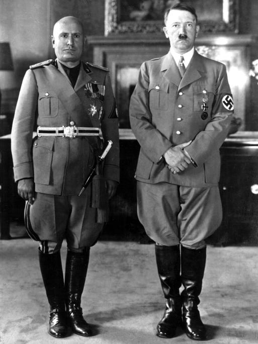 Hitler und Mussolini stehen nebeneinander. Sie tragen Uniform und schauen streng in die Kamera.