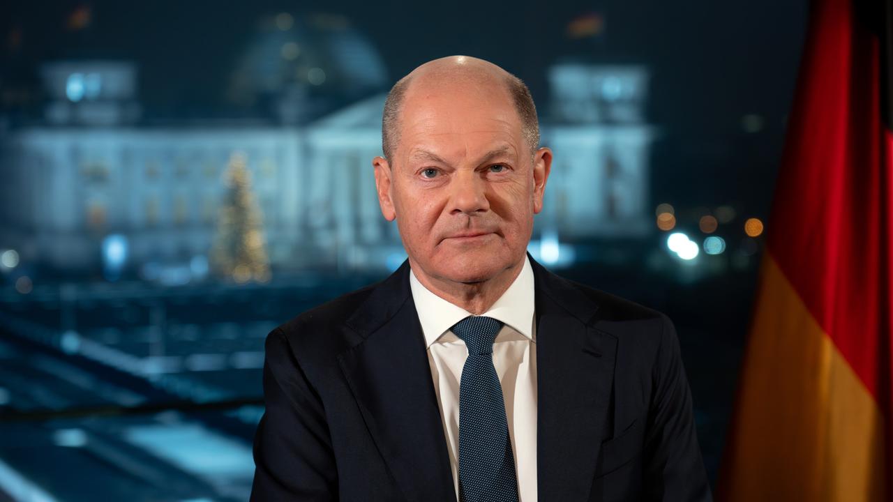 Bundeskanzler Olaf Scholz (SPD) sitzt während eines Fototermins nach der Aufzeichnung seiner Neujahrsansprache im Kanzleramt vor der Kulisse des von Scheinwerfern angestrahlten Reichstages.