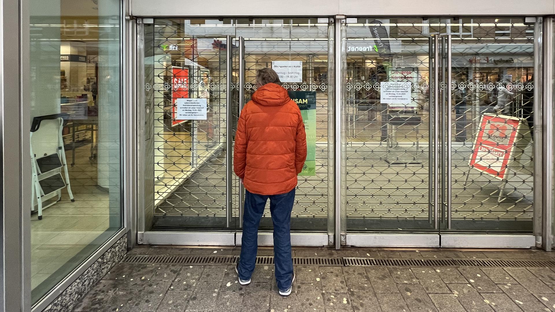 Ein Mann in oranger Jacke steht vor einer geschlossenen Filiale des Warenhauskonzerns Galeria Karstadt Kaufhof. 
