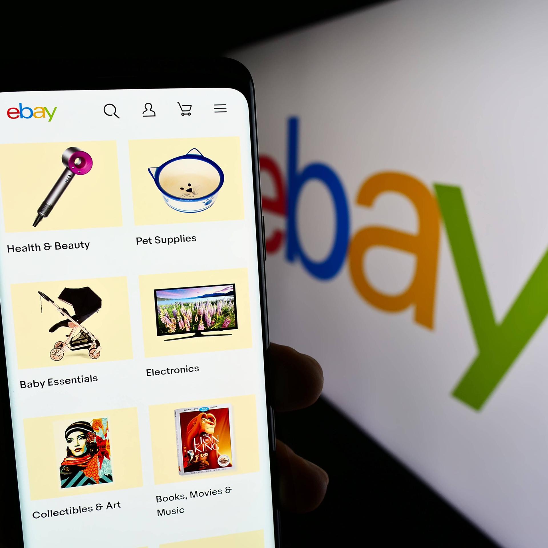 Eine Person hält ein Smartphone mit der Ebay-App. Im Hintergrund das Ebay-Logo.