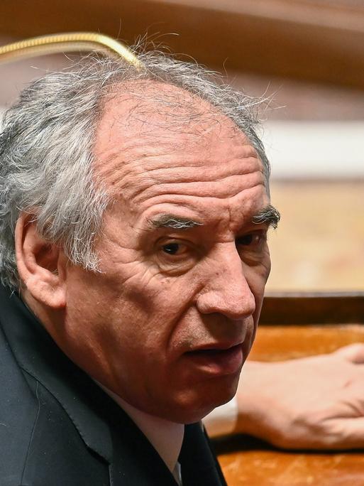 Ein Mann sitzt im französischen Parlament an einem Pult und blickt sich um. Es ist Premier Francois Bayrou.