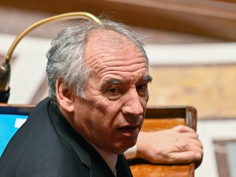 Ein Mann sitzt im französischen Parlament an einem Pult und blickt sich um. Es ist Premier Francois Bayrou.