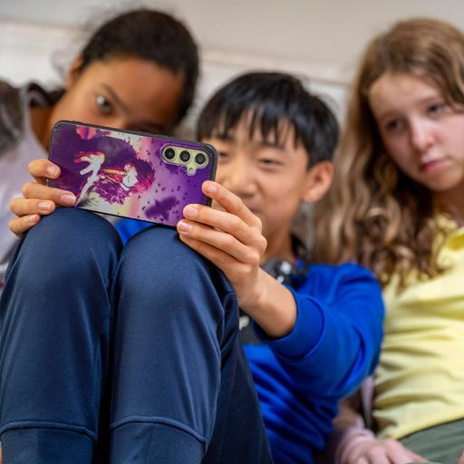 Zwei Mädchen und ein Junge sitzen dicht nebeneinander auf der Couch und machen mit einem Smartphone ein Selfie von sich