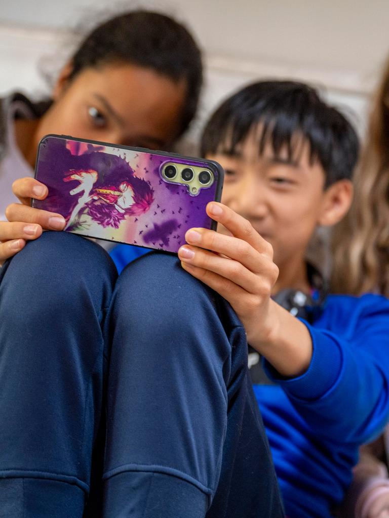 Zwei Mädchen und ein Junge sitzen dicht nebeneinander auf der Couch und machen mit einem Smartphone ein Selfie von sich