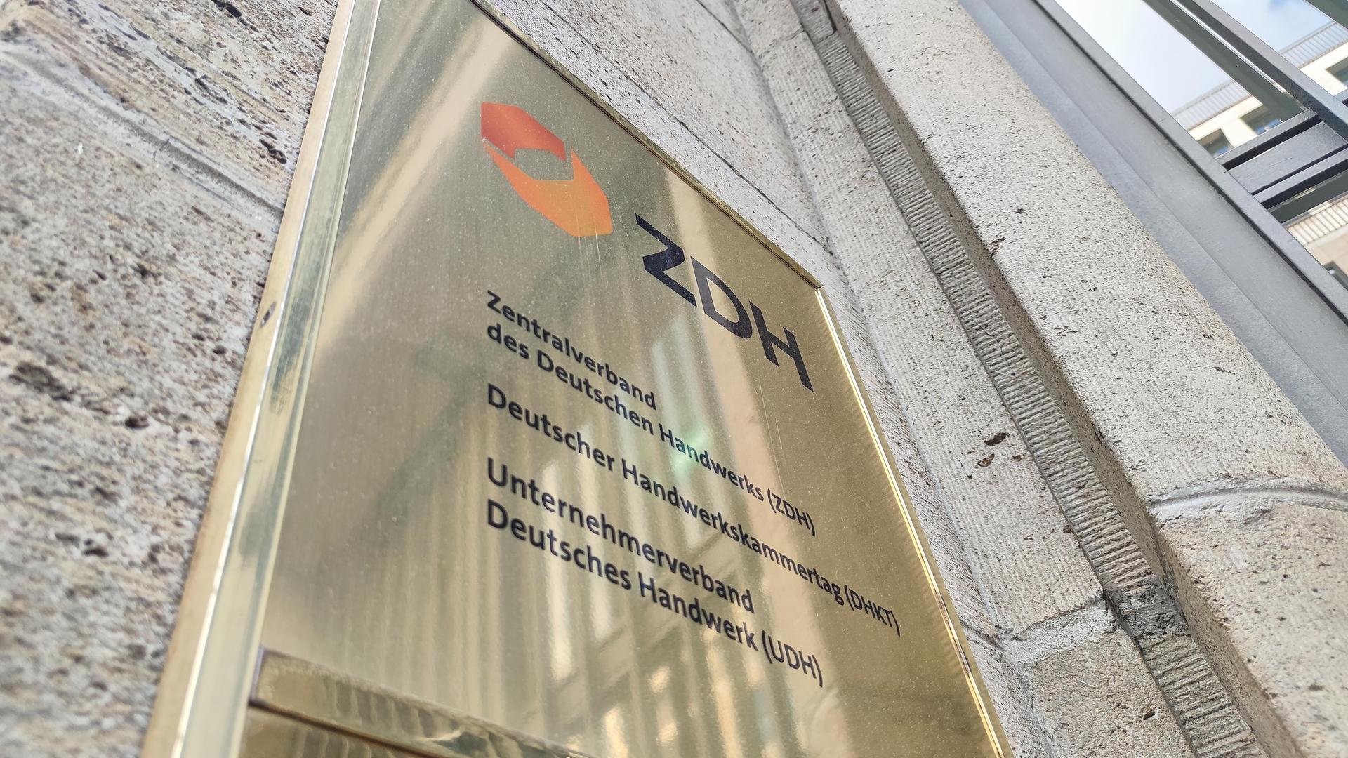 Blick von schräg unten auf das goldfarbene Schild an der Hausfassade. Darauf stehen auch die Namen zweier weiterer Handwerksverbände. 