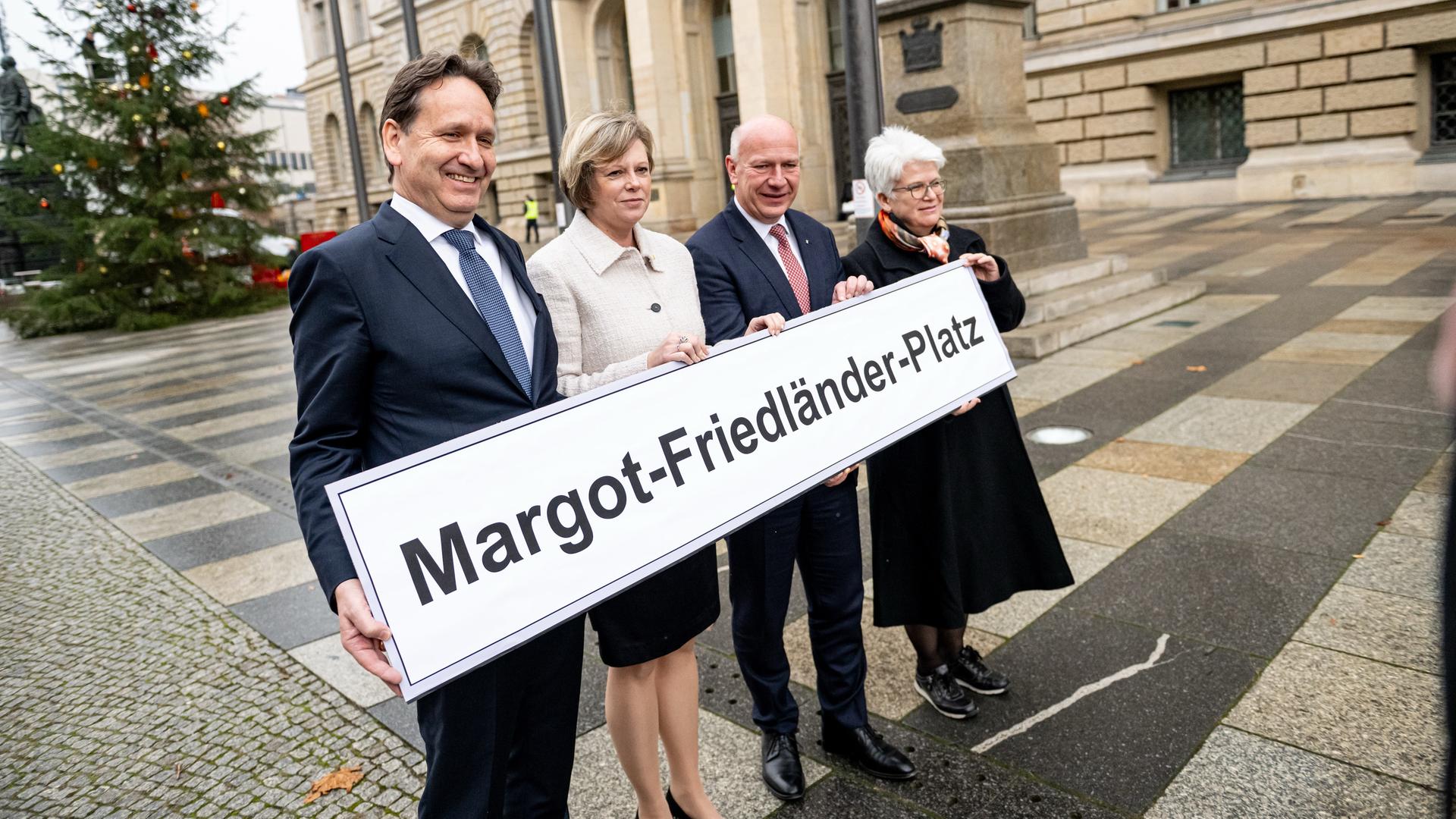 Die beiden und zwei weitere Personen stehen auf dem Platz und halten gemeinsam ein großes Schild mit dem neuen Namen vor sich.