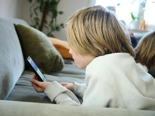 Ein Junge liegt auf einem Sofa und guckt auf sein Smartphone. (gestellte Szene)