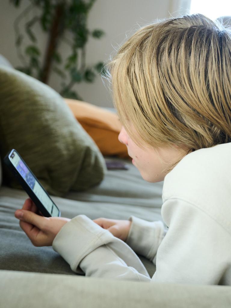 Ein Junge liegt auf einem Sofa und guckt auf sein Smartphone. (gestellte Szene)