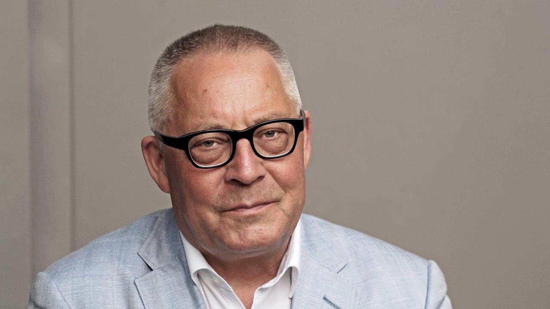 Ein Porträt von Karl Schlögel. Er sitzt in weißem Hemd und hellblauem Sakko vor einer grauen Wand und schaut in die Kamera. Ein Porträt von Karl Schlögel. Er sitzt in weißem Hemd und hellblauem Sakko vor einer grauen Wand und schaut in die Kamera.