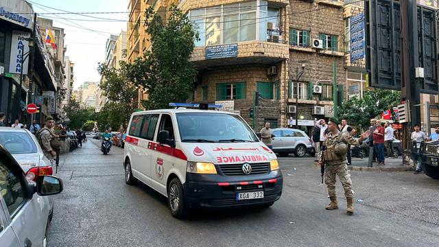 Ein Krankenwagen fährt auf einer Straße in Beirut. Mehrere Polizisten und Menschen stehen am Straßenrand.