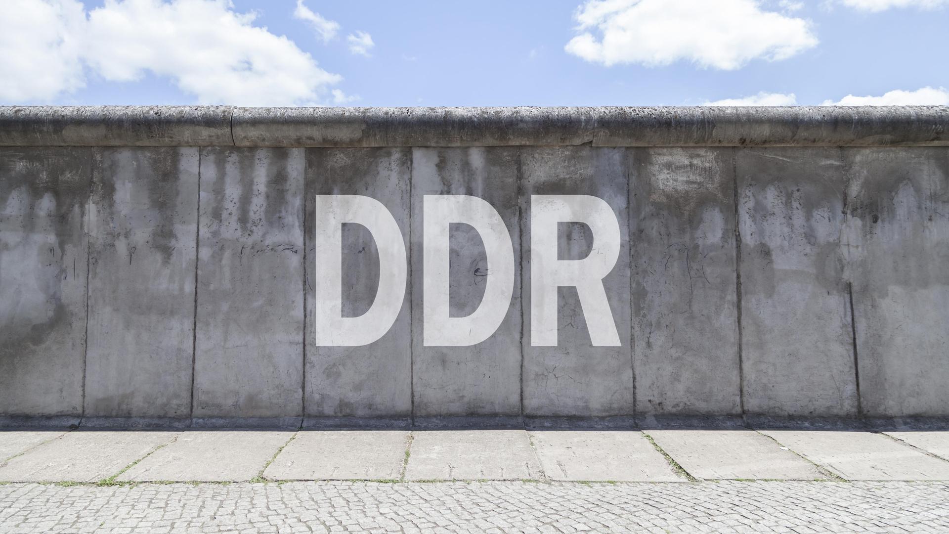 Fotomontage: Ein Stück Berliner Mauer in Berlin. Darauf der Schriftzug DDR.