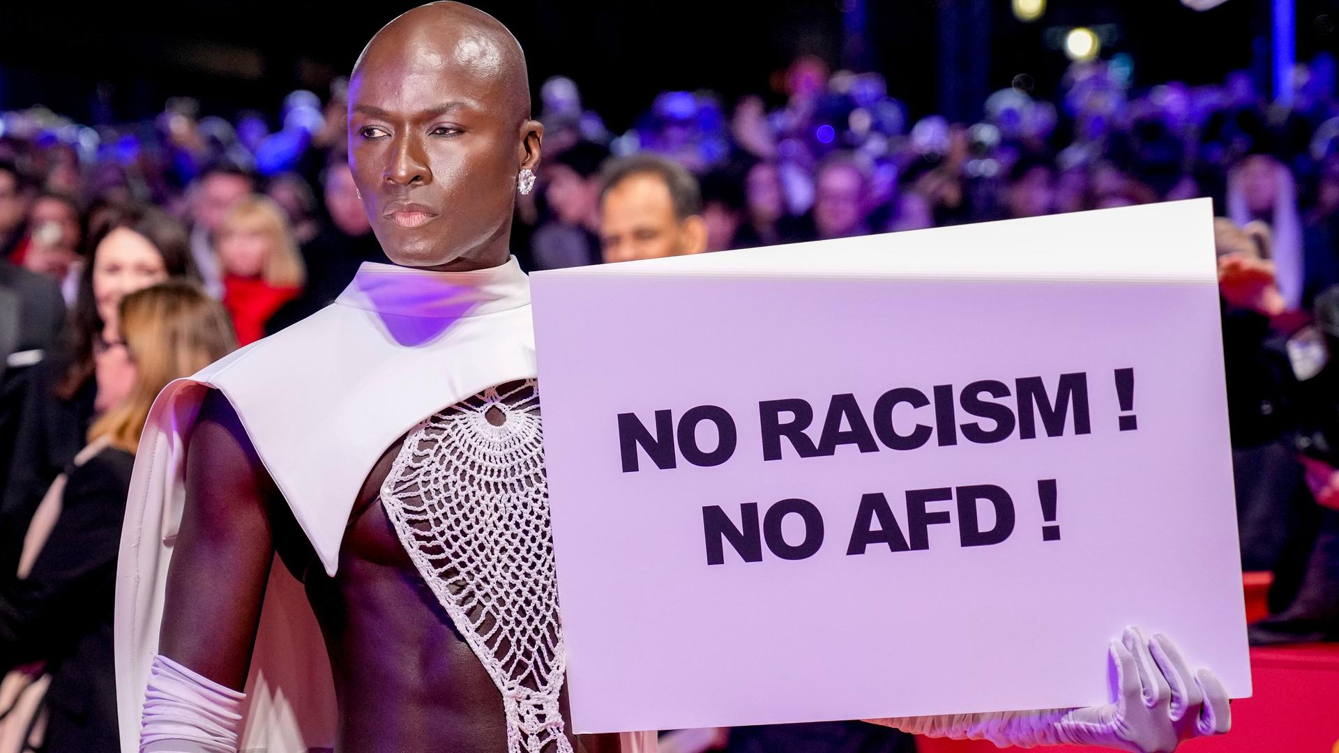 Protest gegen die AfD auf dem Roten Teppich bei der Eröffnung der Berlinale. Ein Mann hält ein Schild auf dem steht "NO RACISM! NO AFD!"