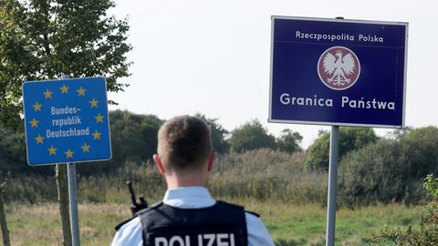 Bei einer flexiblen Schwerpunktkontrolle unmittelbar an der deutsch-polnischen Grenze in der Nähe des ehemaligen Grenzübergang Linken steht ein Bundespolizist vor den Schildern für Deutschland und Polen. 