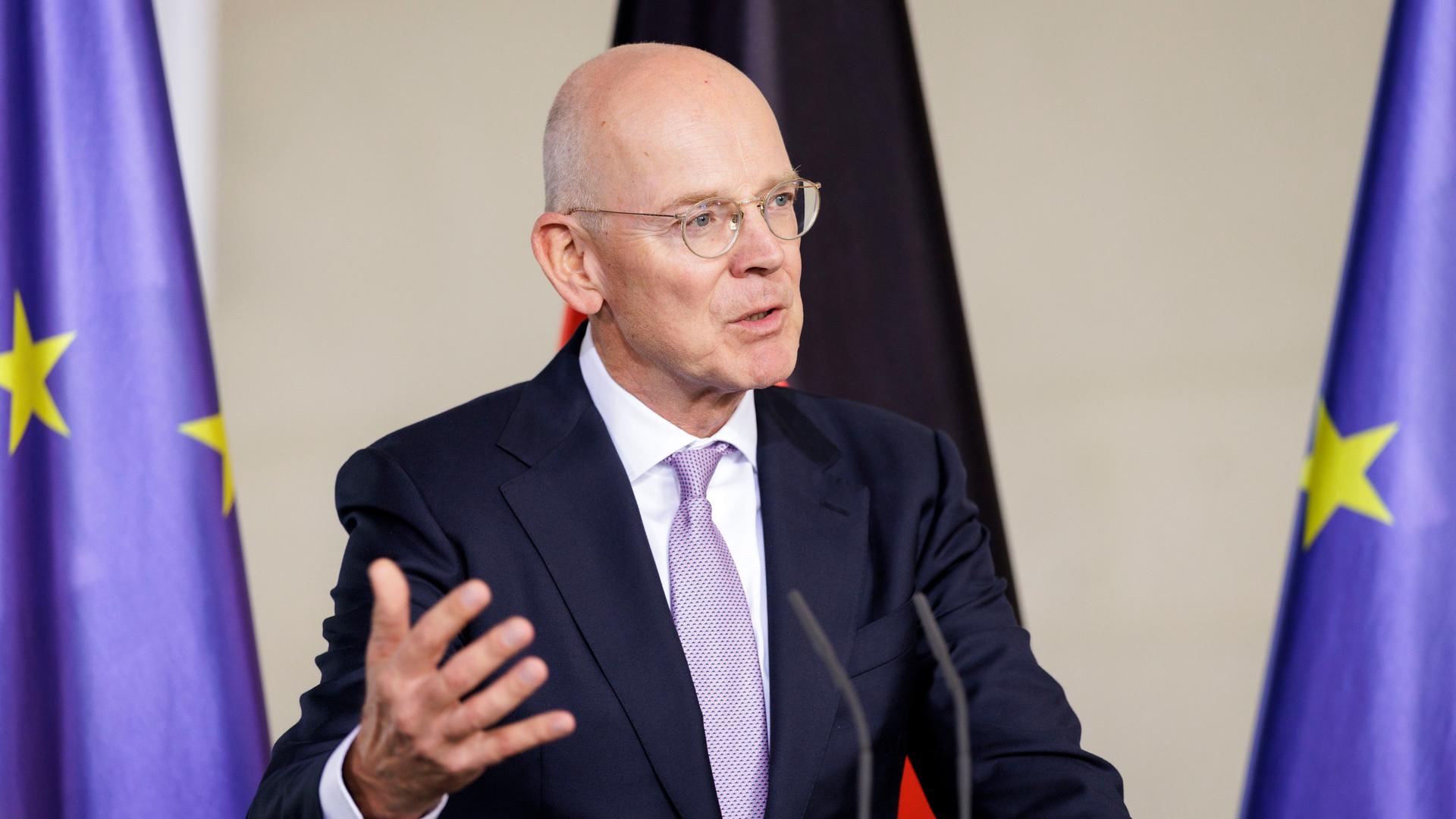 Martin Blessing steht an einem Rednerpult und spricht in in Mikrofon. Im Hintergrund die deutsche und die europäische Flagge.