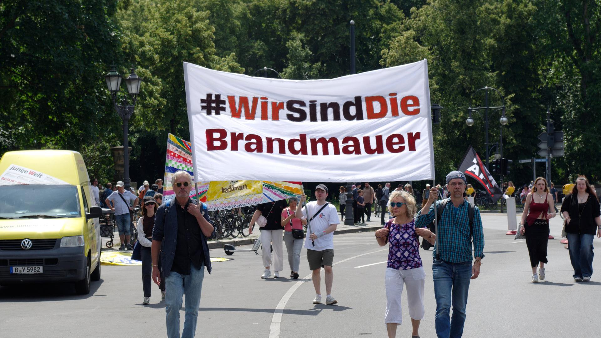 Ein Demonstration gegen Rechtsextremismus auf einer Straße in Berlin. Einige Menschen laufen auf der Straße und halten ein Transparent hoch mit der Aufschrift "Wir sind die Brandmauer!"