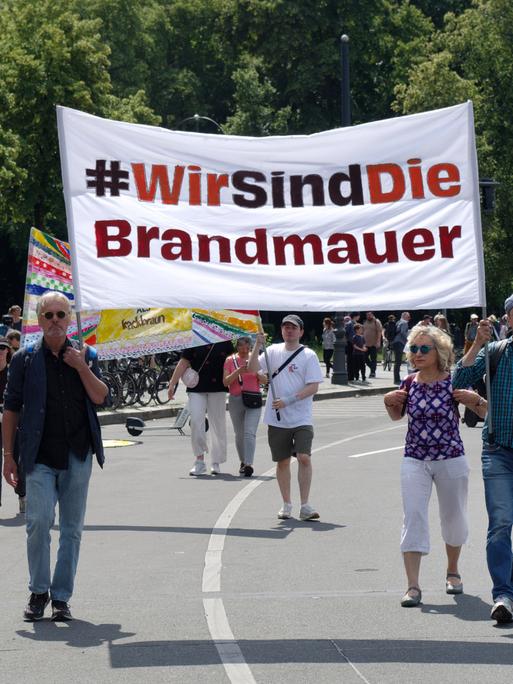 Ein Demonstration gegen Rechtsextremismus auf einer Straße in Berlin. Einige Menschen laufen auf der Straße und halten ein Transparent hoch mit der Aufschrift "Wir sind die Brandmauer!"