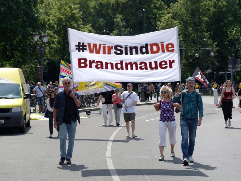 Ein Demonstration gegen Rechtsextremismus auf einer Straße in Berlin. Einige Menschen laufen auf der Straße und halten ein Transparent hoch mit der Aufschrift "Wir sind die Brandmauer!"