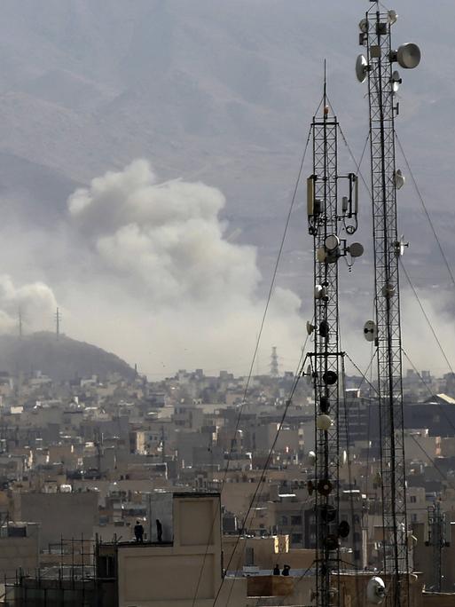 Über den Dächern von Teheran steigen Rauchwolken auf, im Vordergrund sind Sendemasten zu sehen.