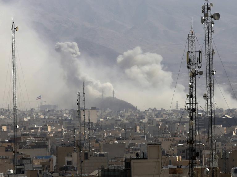 Über den Dächern von Teheran steigen Rauchwolken auf, im Vordergrund sind Sendemasten zu sehen.