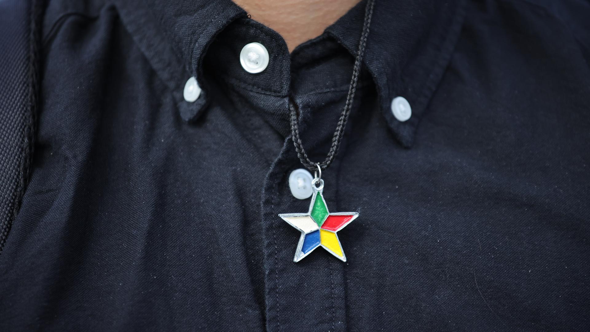 Eine Person in schwarzem Hemd trägt einen Stern mit fünf verschieden farbigen Spitzen Eine Person in schwarzem Hemd trägt einen Stern mit fünf verschieden farbigen Spitzen