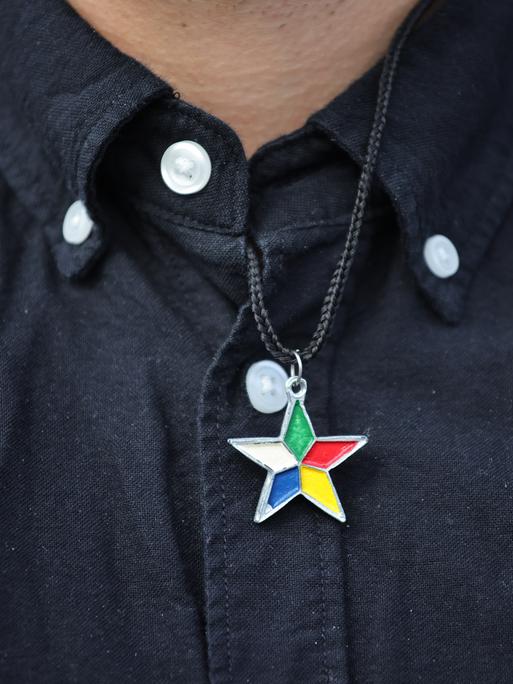 Eine Person in schwarzem Hemd trägt einen Stern mit fünf verschieden farbigen Spitzen