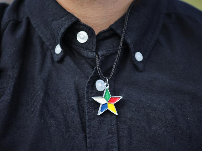 Eine Person in schwarzem Hemd trägt einen Stern mit fünf verschieden farbigen Spitzen