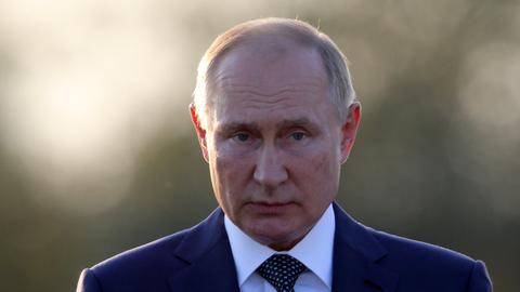Portrait von Wladimir Putin, der mit gerunzelter Stirn leicht nach unten schaut. Im Hintergrund sieht man in der Unschärfe Bäume.