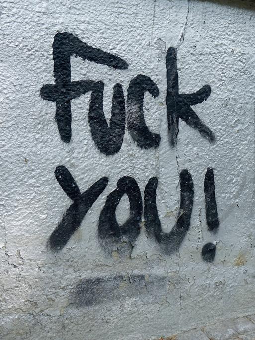 Schwarzer Schriftzug "Fuck you" auf einer Hauswand