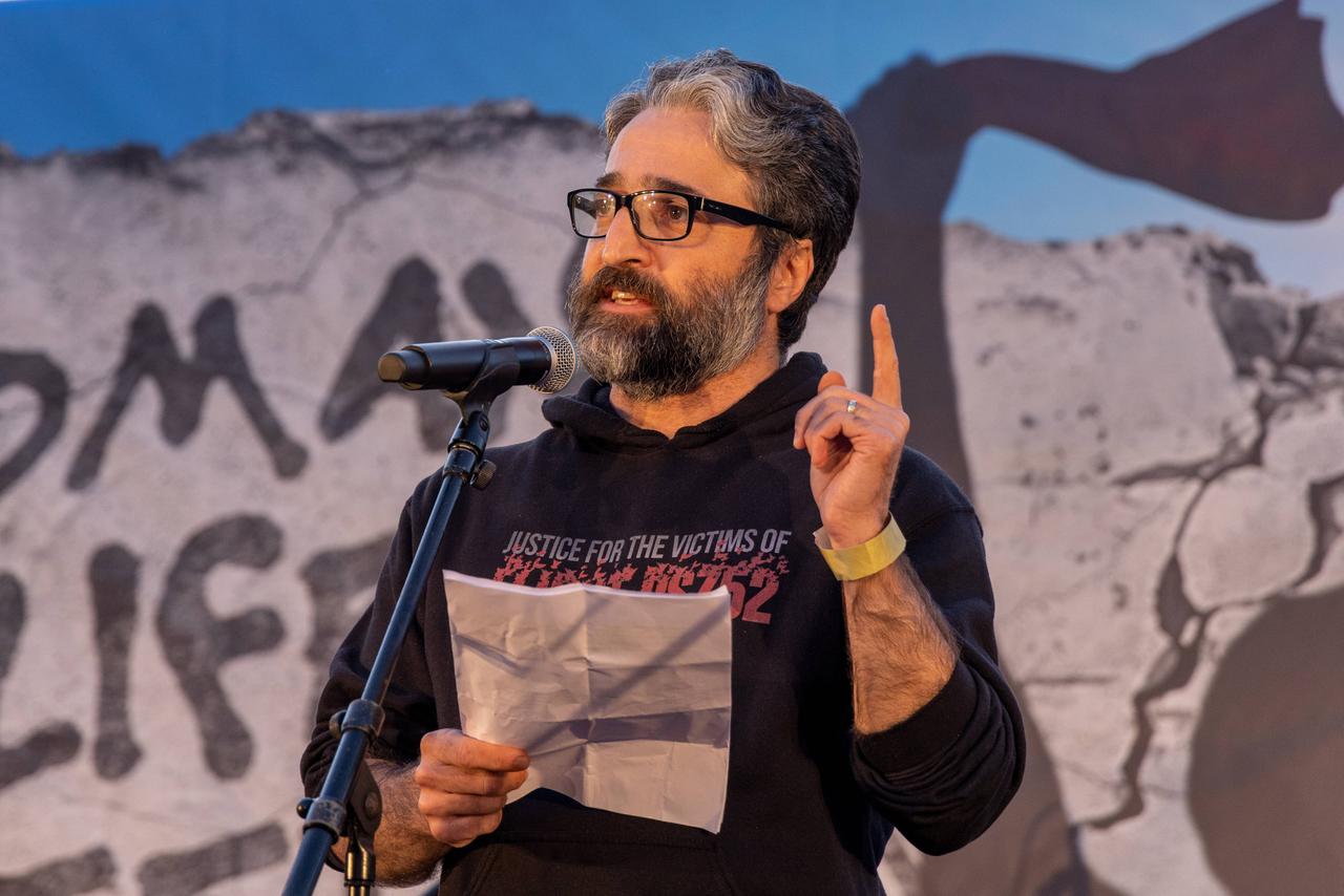 Der iranische Aktivist Hamed Esmaeilion spricht auf einer Demonstration aus Solidarität mit den Protestierenden im Iran in Berlin. Er steht vor einem Mikrofon mit Zetteln in der Hand und gestikuliert.