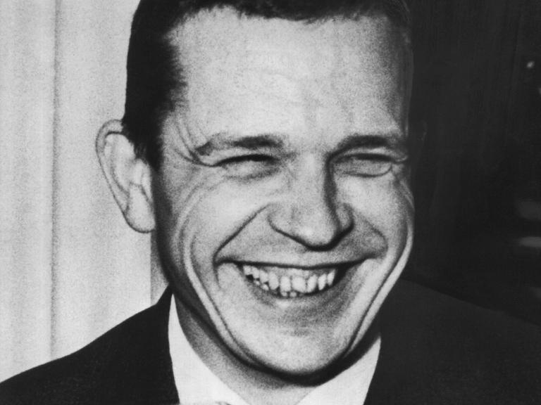 Ein junger Mann auf einer Schwarz-Weiß-Aufnahme: Es ist der Dramatiker Peter Hacks. Er lacht, dabei kommen seine Zähne zum Vorschein, die Augen sind zusammen gekniffen.