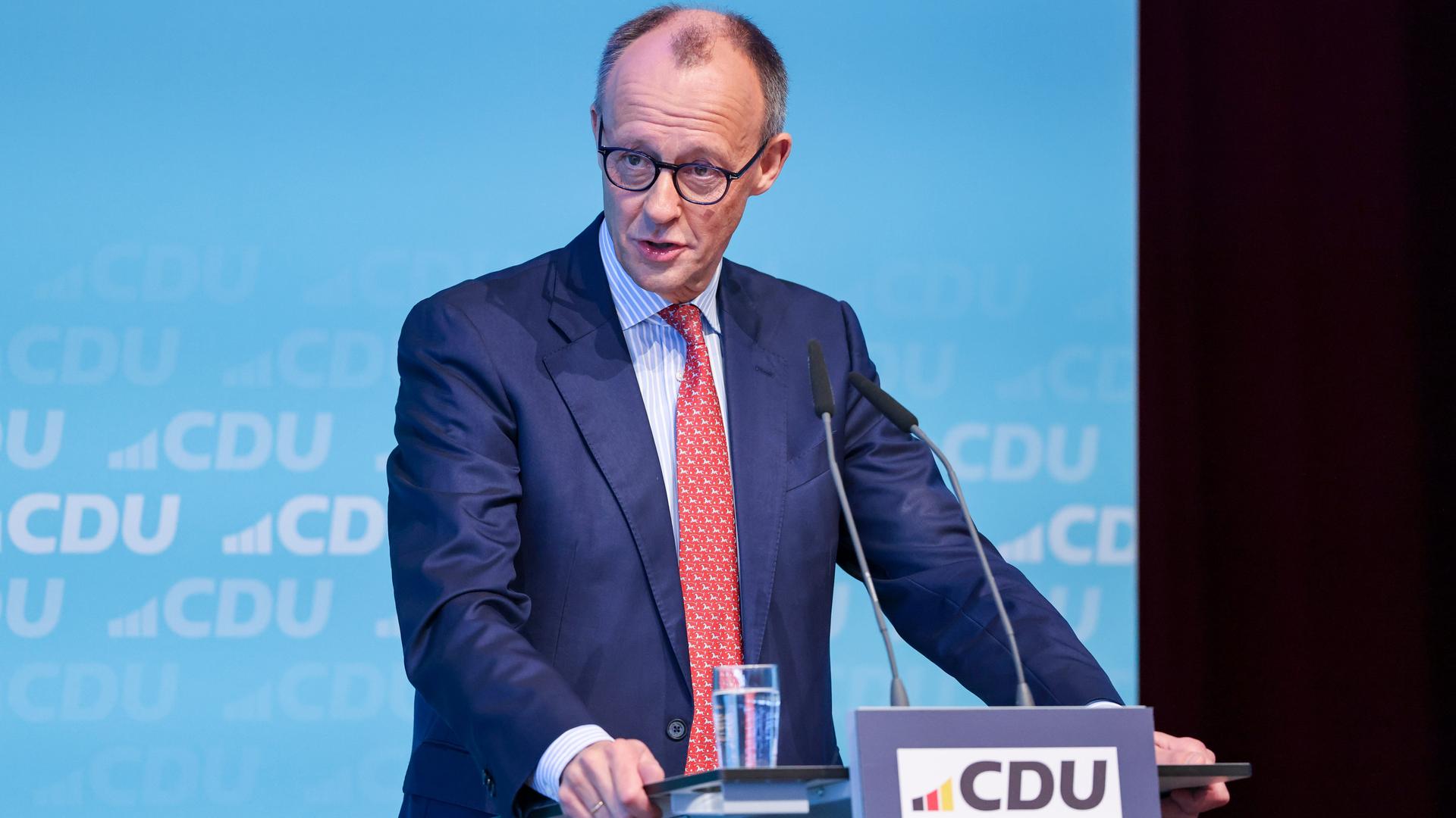 Friedrich Merz steht an einem Redepult und spricht in Mikrofone. Im Hintergrund sind Logos seiner Partei CDU zu sehen.