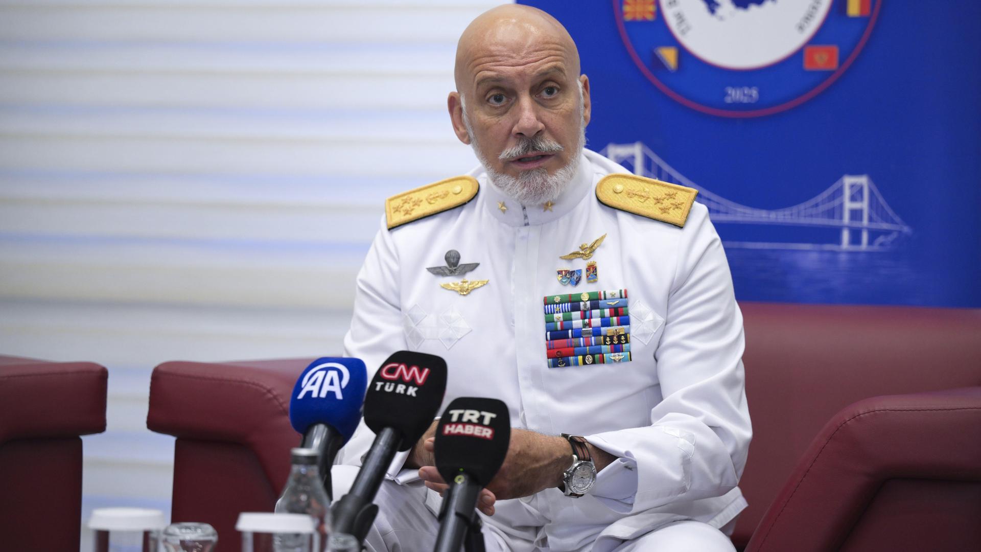 Ds Foto zeigt Admiral Giuseppe Cavo Dragone, er sitz in weißer Uniform vor drei Mikrofonen.