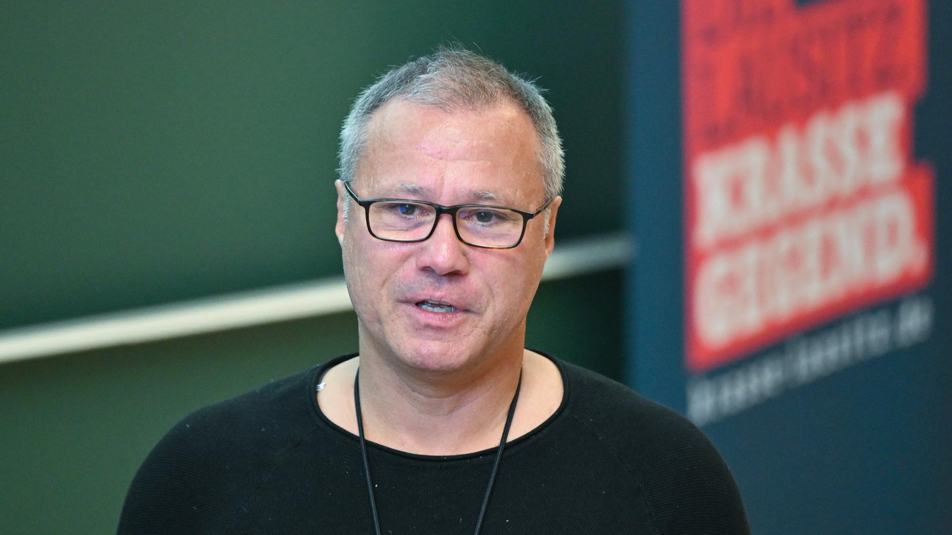 Daniel Ris, der Intendant der Neuen Bühne Senftenberg, mit schwarzem T-Shirt und schwarzer Brille vor schwarzem Hintergrund.