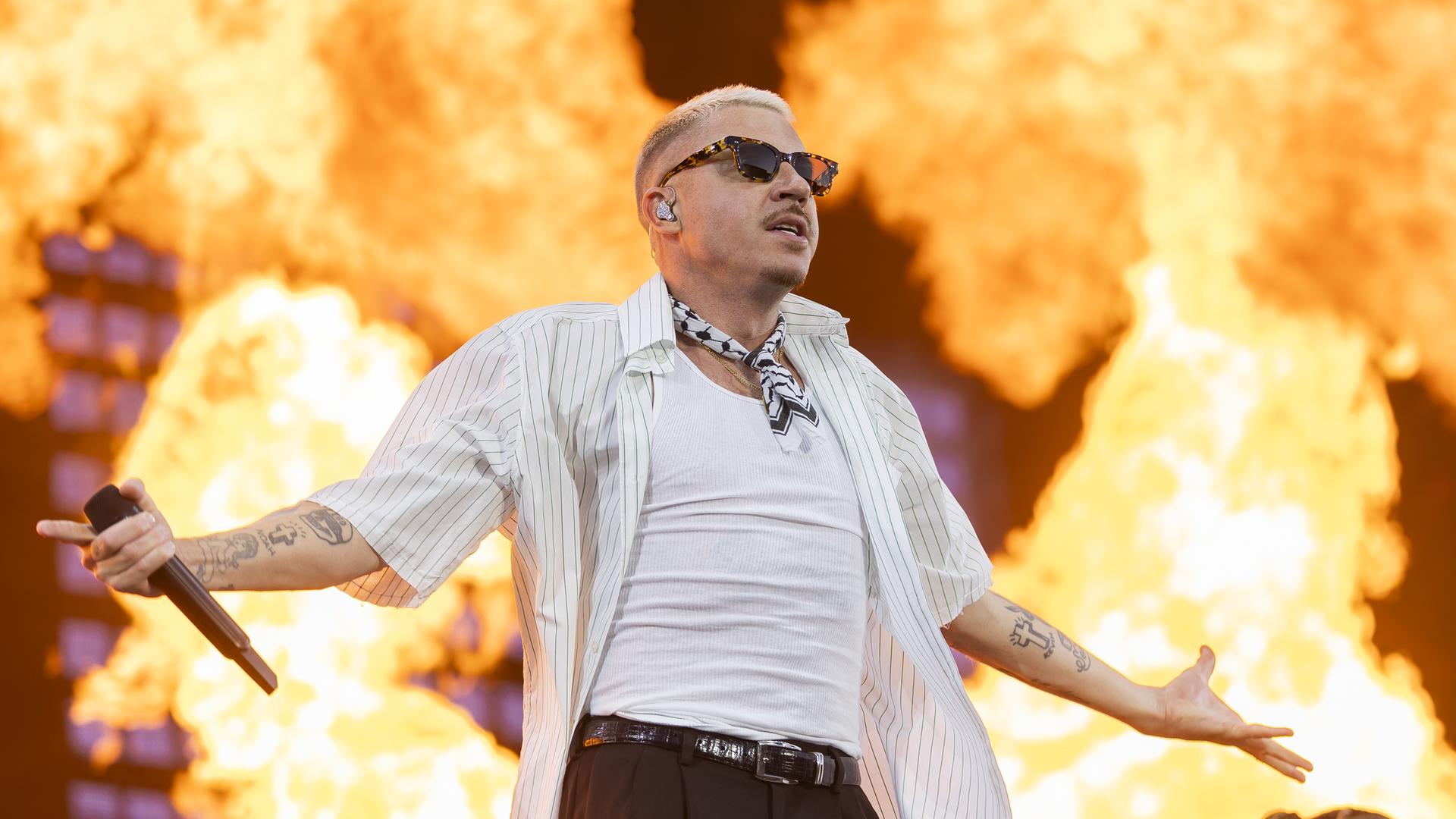 Der US-Rapper Macklemore steht mit ausgebreiteten Armen auf einer Bühne, hinter ihm sind riesige Flammen. Der US-Rapper Macklemore steht mit ausgebreiteten Armen auf einer Bühne, hinter ihm sind riesige Flammen.