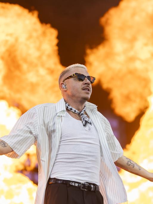 Der US-Rapper Macklemore steht mit ausgebreiteten Armen auf einer Bühne, hinter ihm sind riesige Flammen. Der US-Rapper Macklemore steht mit ausgebreiteten Armen auf einer Bühne, hinter ihm sind riesige Flammen.