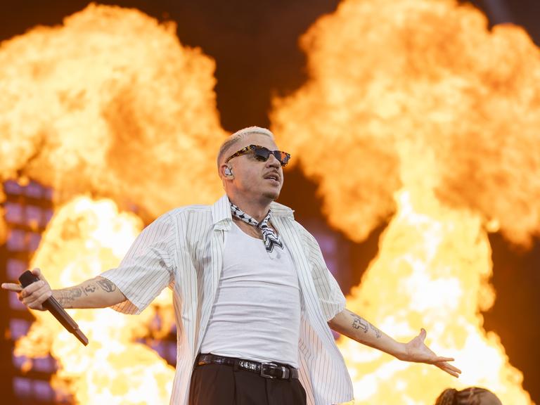 Der US-Rapper Macklemore steht mit ausgebreiteten Armen auf einer Bühne, hinter ihm sind riesige Flammen. Der US-Rapper Macklemore steht mit ausgebreiteten Armen auf einer Bühne, hinter ihm sind riesige Flammen.
