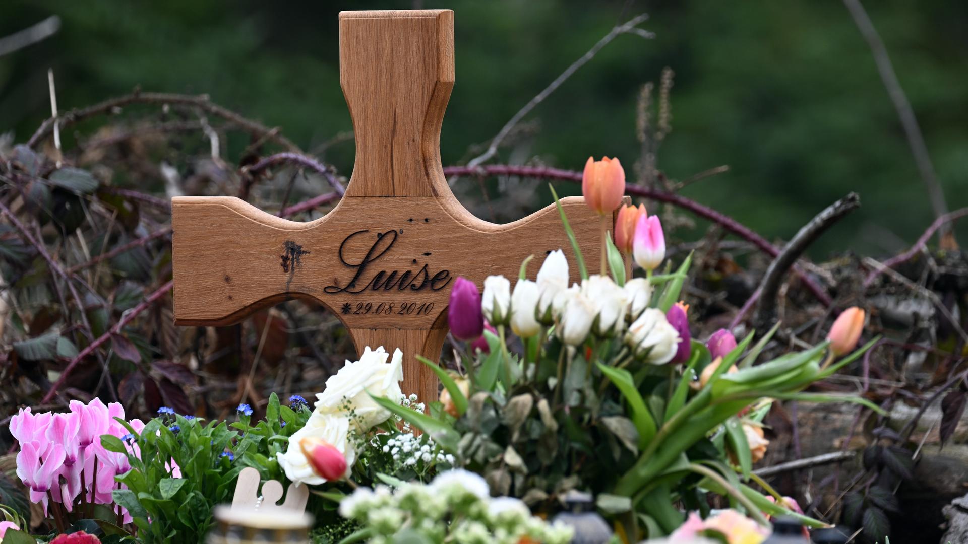 Ein Holzkreuz, zahlreiche Blumen, Kuscheltiere und Kerzen liegen am Tatort. 