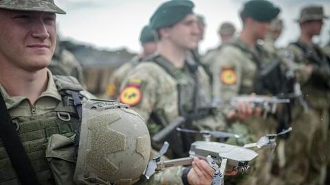 Ein Soldat hält eine Drohne in der Hand. Im Hintergrund sind weitere Soldaten zu sehen.