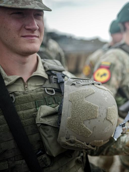 Ein Soldat hält eine Drohne in der Hand. Im Hintergrund sind weitere Soldaten zu sehen.